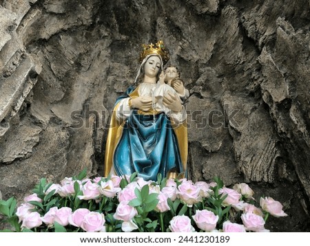 Photo of Virgin Mary and baby Jesus statue with a foreground of pink roses in the man-made cave. Low angle photography