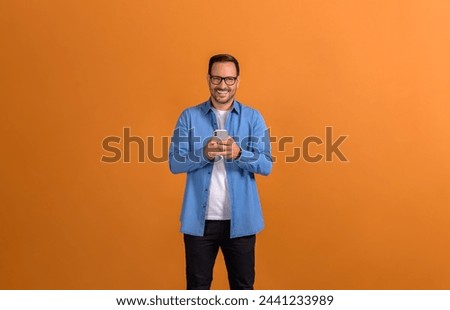 Portrait of happy confident young entrepreneur texting over smartphone on isolated orange background