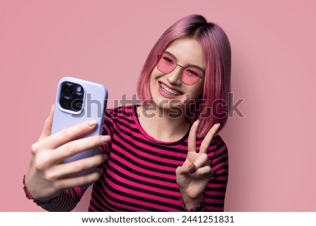 Portrait photo - pleasant pink haired woman in braces wear sunglasses eye glasses making taking selfie or show her viewer positive result with cell phone smartphone, v-sign gesture isolated background