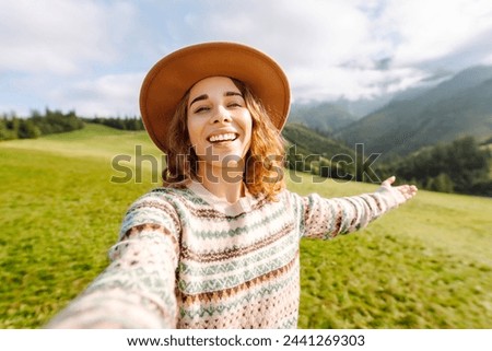 Happy female tourist  is making a selfie or technology video call to friends or relatives just reached a peak while hiking in the middle of hills surrounded by green nature.