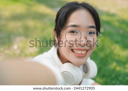 A young woman wearing glasses and a white shirt is smiling for a picture. She is wearing headphones and she is enjoying herself