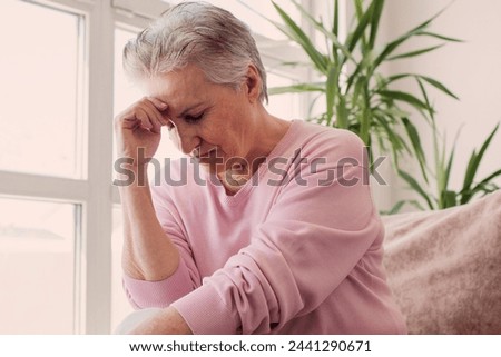 Mature woman sitting on the sofa feeling sad and alone. Upset 60s female in living romm at home
