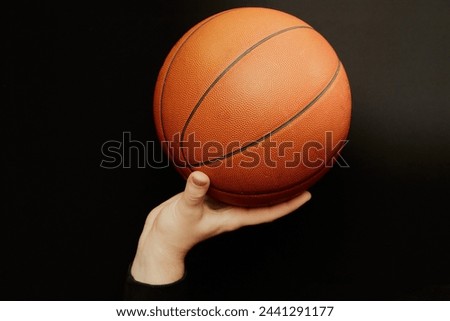 A basketball ball is held by a hand ready to throw on a black background close-up blur, sports background