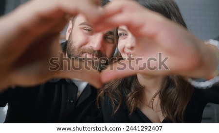 Close-up portrait of young happy couple making heart shape with joined fingers and looking at camera with smiles in between.