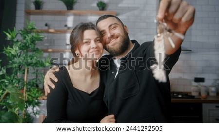 Newly married young couple sitting in kitchen smile look at camera husband show of keys from new house. Proud homeowners, rented flat, loan mortgage concept. Royalty-Free Stock Photo #2441292505