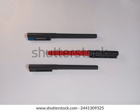 Showcases three ballpoint pens, each with distinct features. Black, Red Barrel, Blue Cover on Grey Surface. Ideal for illustrating office supplies, writing tools, or stationery concepts.