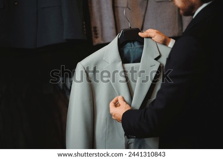 Store classic clothes for men. Smiling businessman in glasses chooses to buy suit jacket in shop