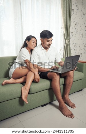 Couple have video chat with his friends while sitting on sofa at home. Browsing social network
