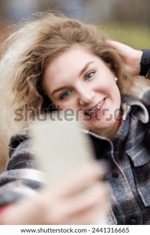 A cheerful young woman with dental braces is take a selfie with her smartphone during the fall season in a park.