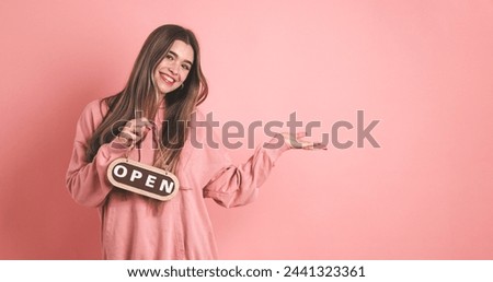Happy female owner holding open sign and gesturing in pink studio