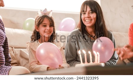 Girl blowing out the candles on her birthday cake sitting on a sofa