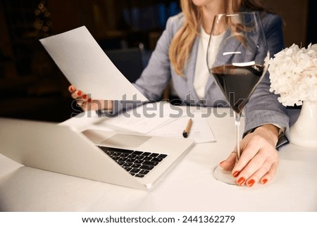 Lady enjoys glass of wine while working on her laptop