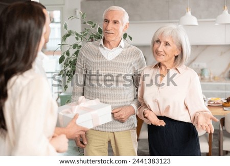 Hospitable smiling elderly couple warmly welcoming adult daughter with husband bringing gift to parents for family celebration in comfortable pleasant atmosphere at home Royalty-Free Stock Photo #2441383123