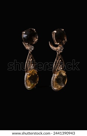 Golden earrings with citrine, a mineral of golden, yellow color. Transparent, precious stone. Against a black background Royalty-Free Stock Photo #2441390943