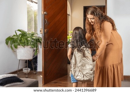 Latin mother and daughter getting ready to go to school next to the door in the entrance hall of the house