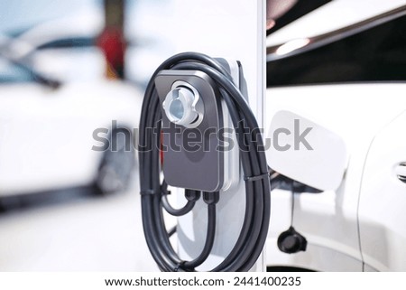 White Electric Car charging at dual plug-in EV supercharger station against blurred cars background. Royalty-Free Stock Photo #2441400235