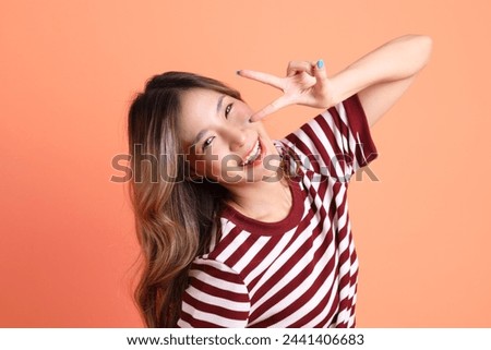 The young Asian woman in casual clothes with gesture of  two finger or V Sign on the orange background 