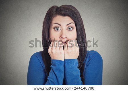 Closeup portrait headshot young unsure hesitant nervous woman biting her fingernails craving for something or anxious, isolated grey wall background. Negative human emotions facial expression feeling 