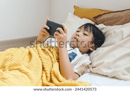 Cute Asian little kid watching video on smartphone alone on the bed.
