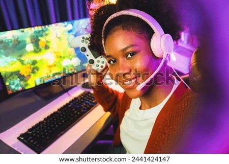 Host channel of gaming streamer, African girl playing fighting Moba game with joystick, wearing pastel headsets with mic, looking at the camera against background in neon color room. Tastemaker.