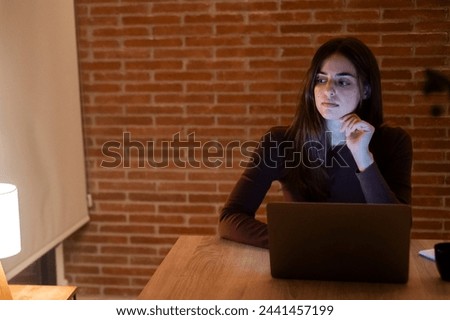 Portrait of young doubts woman using laptop at night, using modern technology havinmg fun with glowing screen in dark office or at home, startup business meeting online with businesswoman