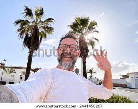 One mature man taking selfie picture in outdoor leisure activity walking on the street in tropical scenic place with palms tree in background. Happy tourist communicate with cellular mobile phone