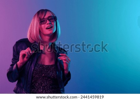 Flirting beautiful blonde woman touch leather jacket sparkly dress trendy sunglasses look aside posing isolated in blue pink color light studio background. Neon party Cyberpunk concept. Copy space