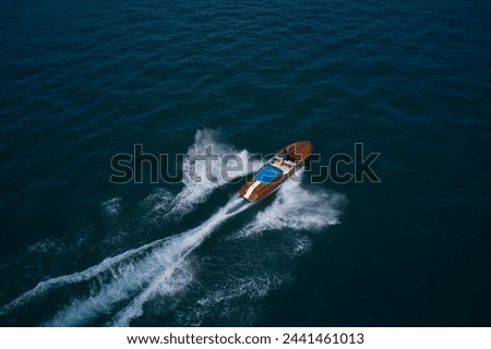 Luxurious wooden boat fast movement on dark water. Classic Italian wooden boat fast moving aerial view. Top view of a wooden powerful motor boat. Royalty-Free Stock Photo #2441461013