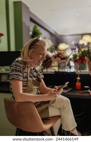 A woman sits in a flower shop and uses her smartphone, surrounded by a variety of flowers