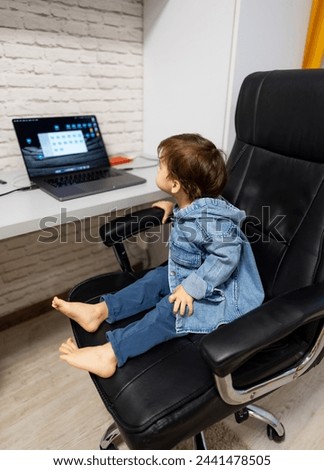Little boy sits in chair and looks at the laptop. The child is watching cartoons on the computer.