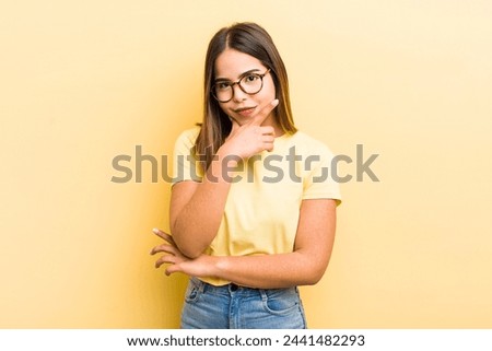 pretty hispanic woman looking serious, thoughtful and distrustful, with one arm crossed and hand on chin, weighting options