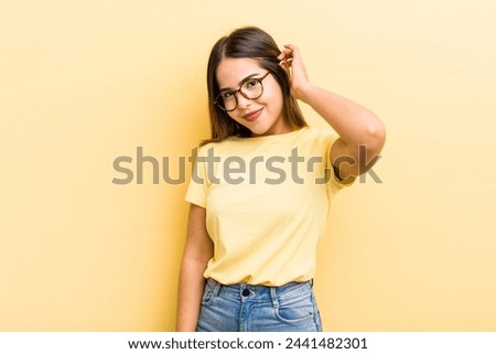 pretty hispanic woman smiling cheerfully and casually, taking hand to head with a positive, happy and confident look