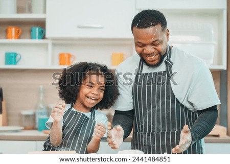 In a home kitchen, black father and his daughter bond over cooking a meal food, their laughter and love filling the air, embodying the joy of African American family life, Father's Day concept Royalty-Free Stock Photo #2441484851