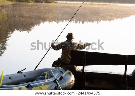 A man sits on a wooden bench and catches a fish with a fishing rod. There is a beautiful forest lake around