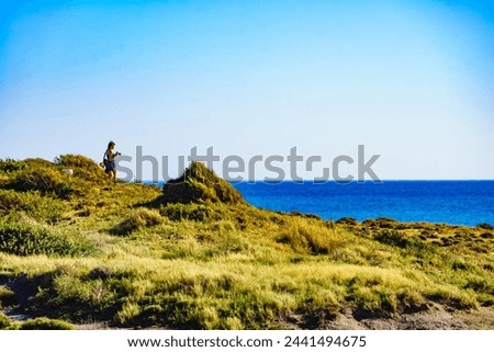 Tourist woman walking on sea shore with camera, taking travel picture from seaside landscape. Calblanque Park in Murcia Spain.