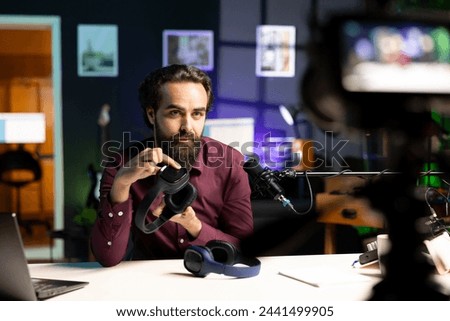 Audiophile reviewing newly launched wireless headphones, testing sound clarity before endorsing them. Tech expert filming internet channel video, checking listening device features Royalty-Free Stock Photo #2441499905