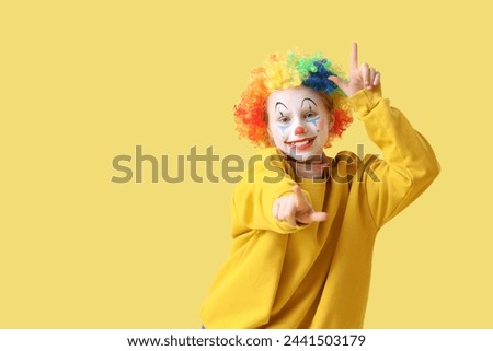 Funny little girl in clown wig showing loser gesture on yellow background. April Fools' Day celebration Royalty-Free Stock Photo #2441503179