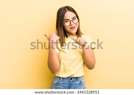 pretty hispanic woman smiling cheerfully and casually pointing to copy space on the side, feeling happy and satisfied