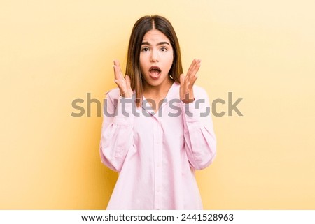 pretty hispanic woman looking shocked and astonished, with jaw dropped in surprise when realizing something unbelievable