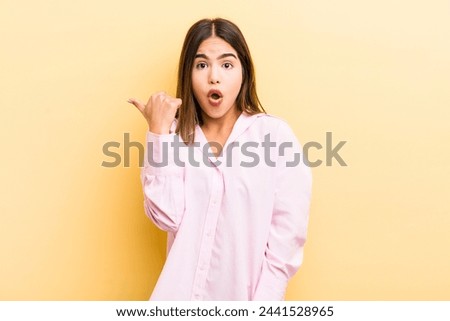 pretty hispanic woman looking astonished in disbelief, pointing at object on the side and saying wow, unbelievable