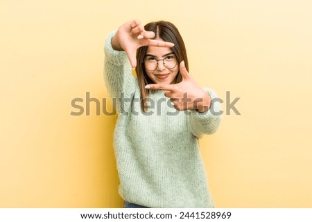 pretty hispanic woman feeling happy, friendly and positive, smiling and making a portrait or photo frame with hands