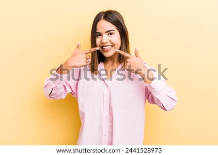 pretty hispanic woman smiling confidently pointing to own broad smile, positive, relaxed, satisfied attitude