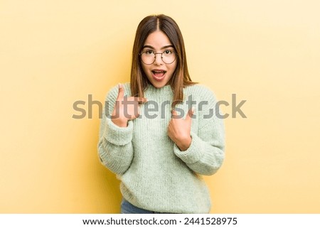 pretty hispanic woman feeling happy, surprised and proud, pointing to self with an excited, amazed look