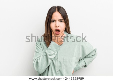 pretty hispanic woman with mouth and eyes wide open and hand on chin, feeling unpleasantly shocked, saying what or wow
