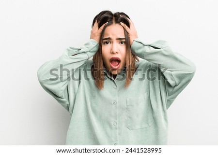 pretty hispanic woman feeling horrified and shocked, raising hands to head and panicking at a mistake