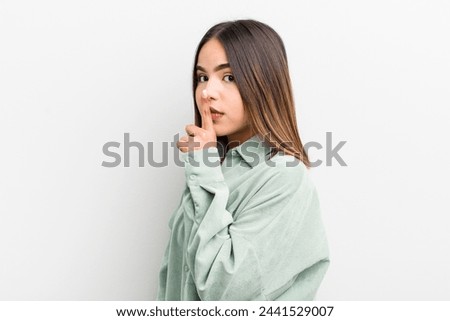 pretty hispanic woman asking for silence and quiet, gesturing with finger in front of mouth, saying shh or keeping a secret