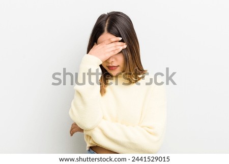 pretty hispanic woman looking stressed, ashamed or upset, with a headache, covering face with hand