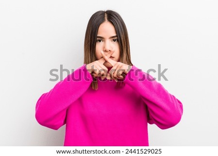 pretty hispanic woman looking serious and displeased with both fingers crossed up front in rejection, asking for silence