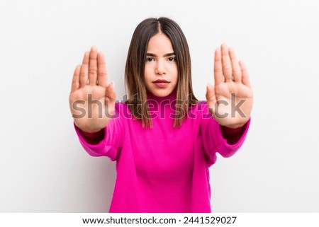 pretty hispanic woman looking serious, unhappy, angry and displeased forbidding entry or saying stop with both open palms