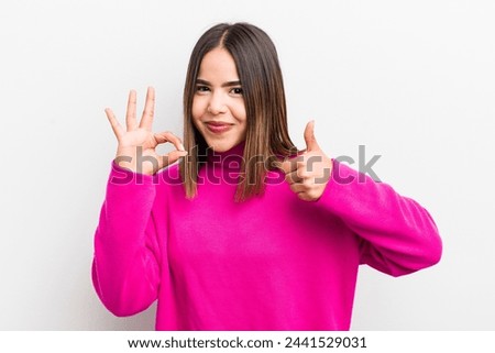 pretty hispanic woman feeling happy, amazed, satisfied and surprised, showing okay and thumbs up gestures, smiling